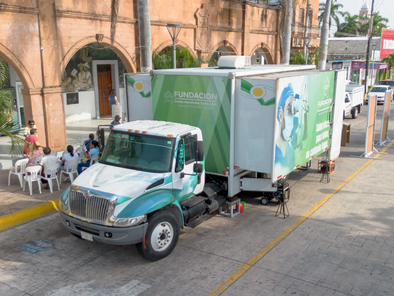 Vista elevada de la unidad móvil estacionada en la calle con pacientes esperando en sillas