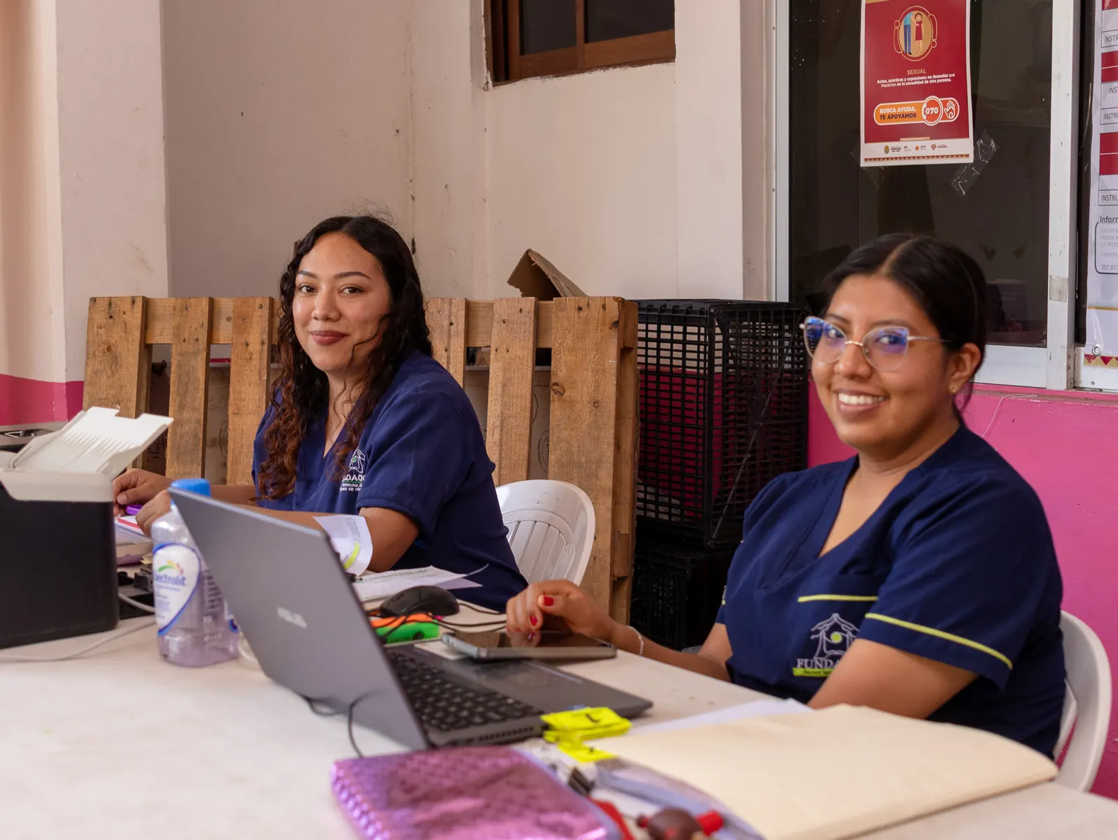 Dos integrantes del equipo con uniforme azul marino sonríen sentadas junto a una laptop