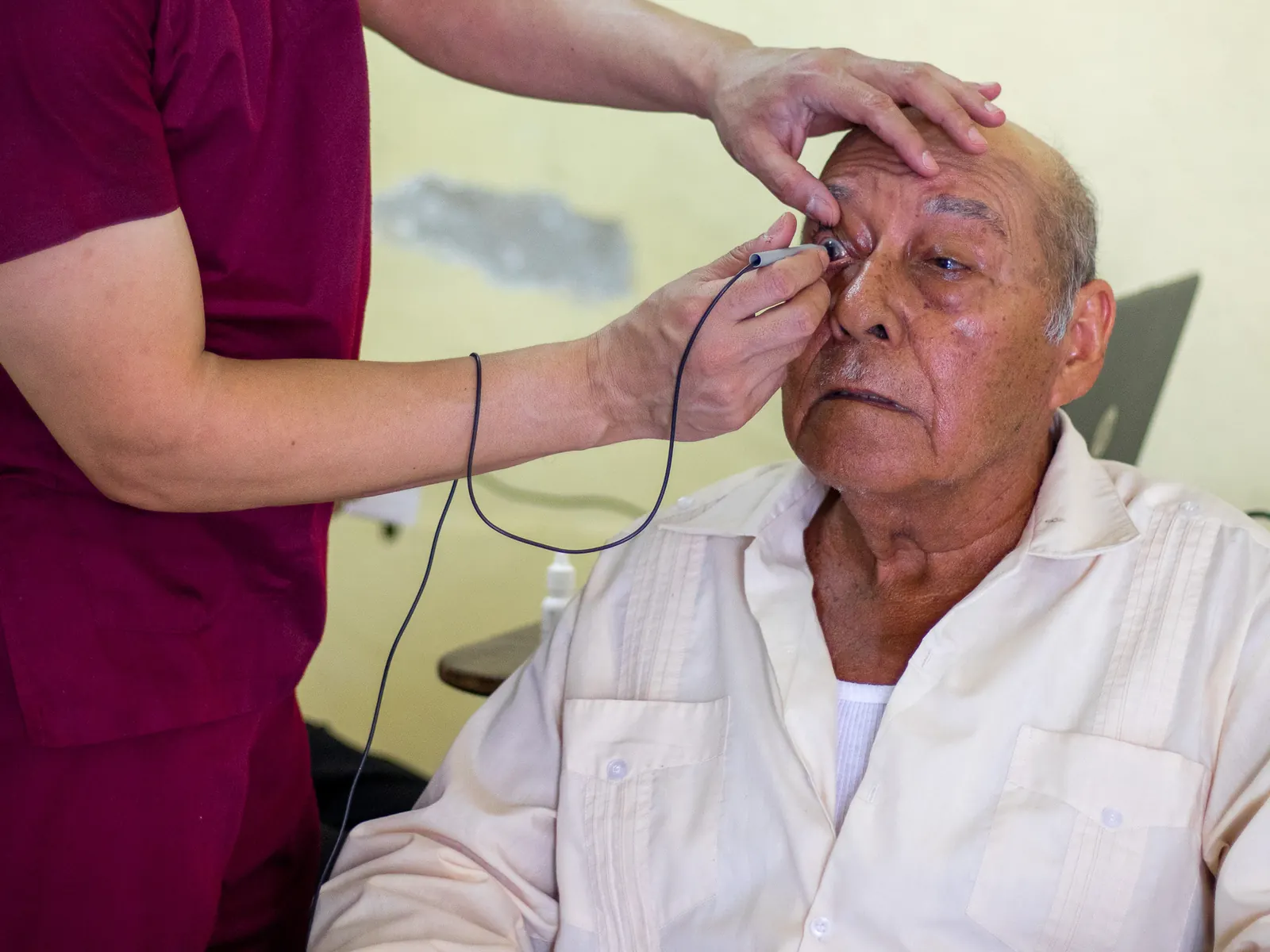Integrante del equipo revisa el ojo de un paciente mayor con un instrumento portátil