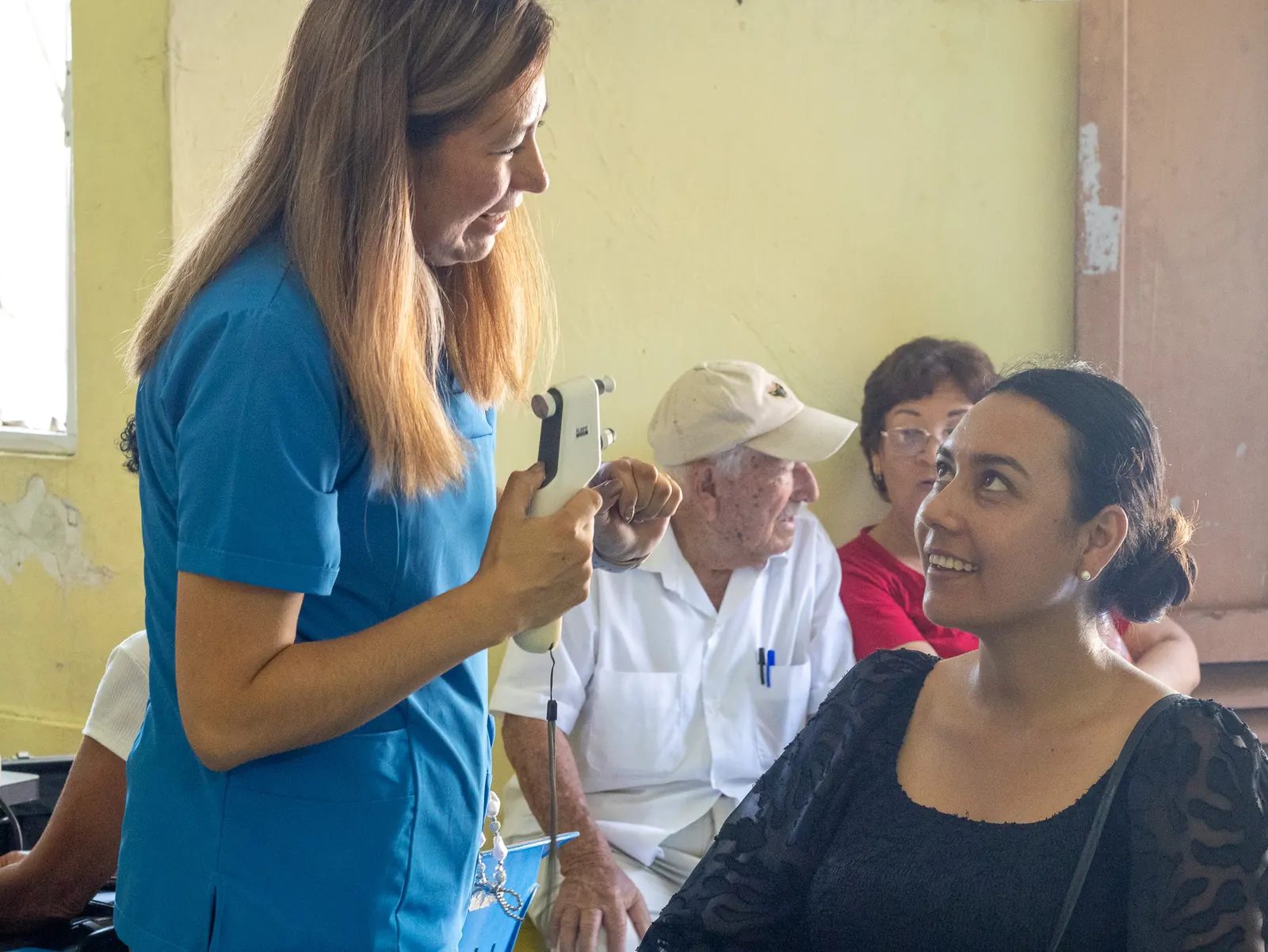 Integrante del equipo sostiene un instrumento portátil frente a pacientes que esperan sentados