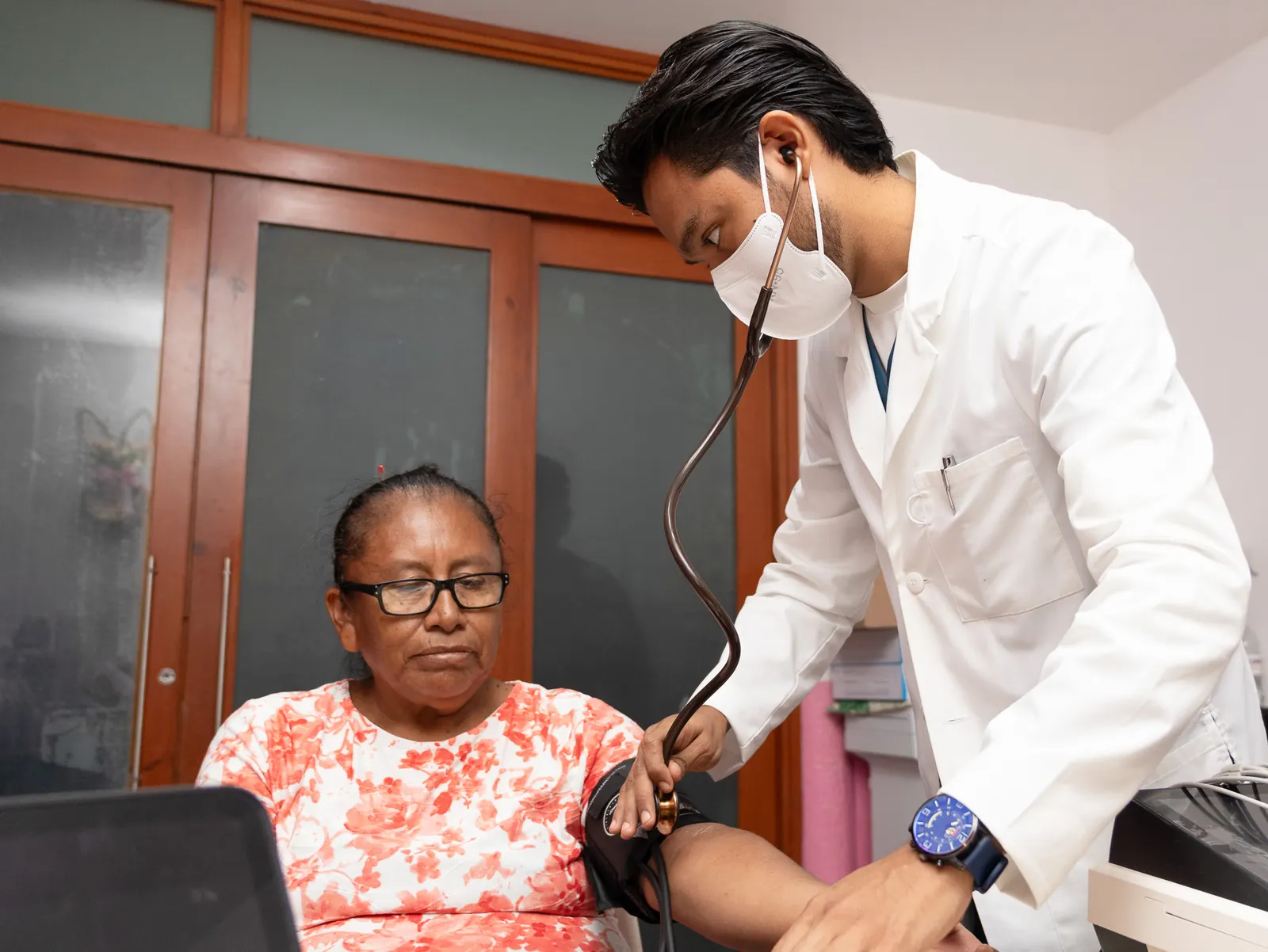 Médico con bata blanca toma la presión arterial a una paciente sentada