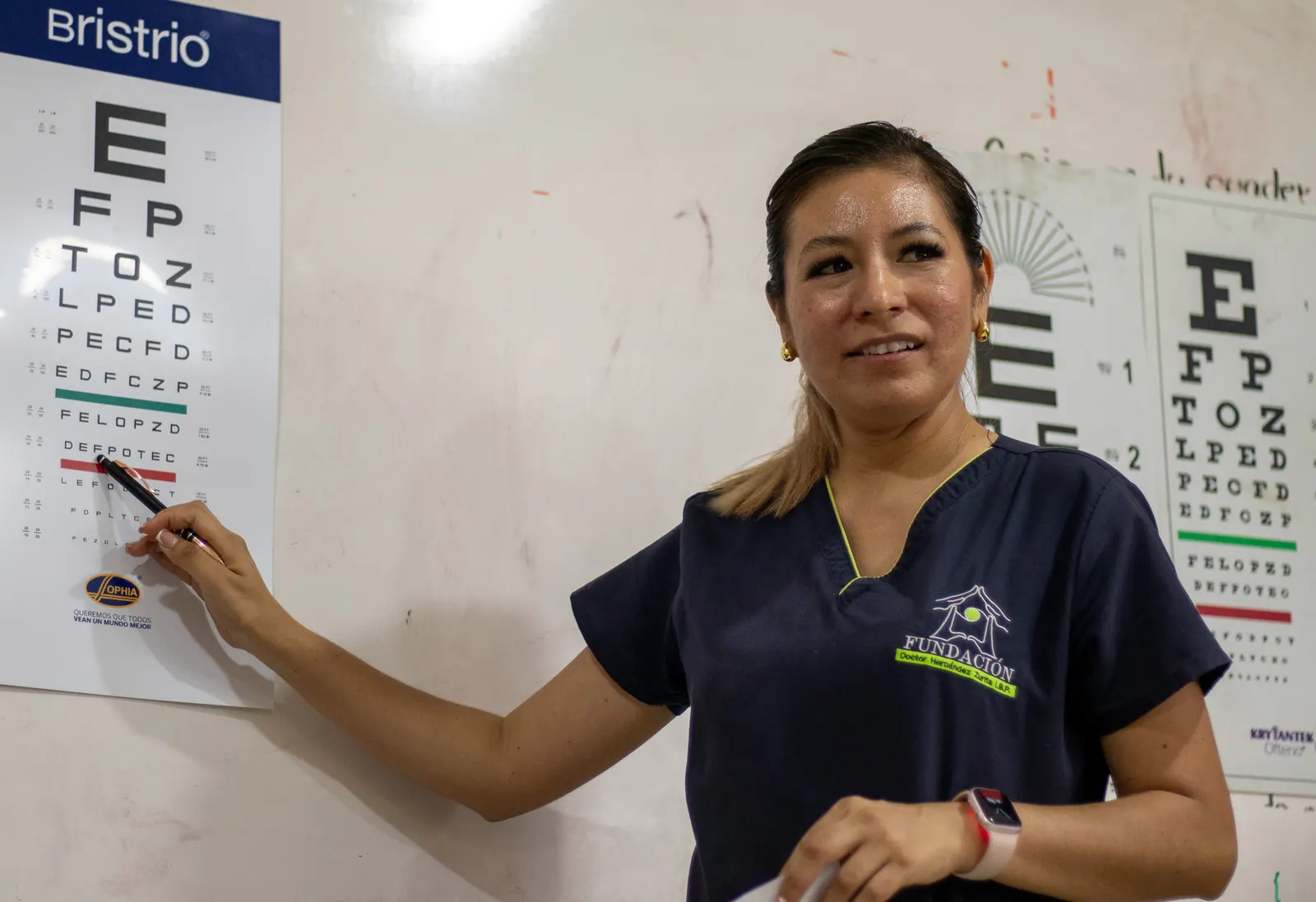 Integrante del equipo señala una cartilla de agudeza visual colgada en la pared