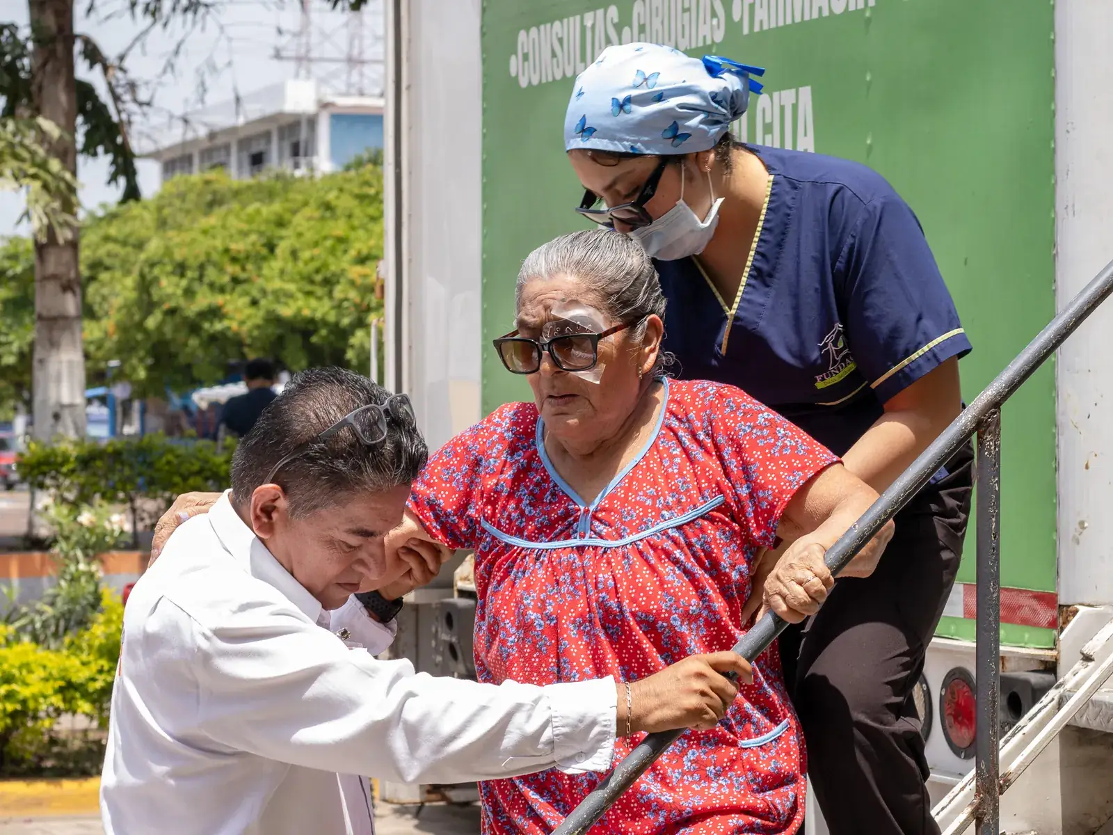 Paciente con protector en el ojo recibe ayuda de dos personas al bajar de la unidad móvil