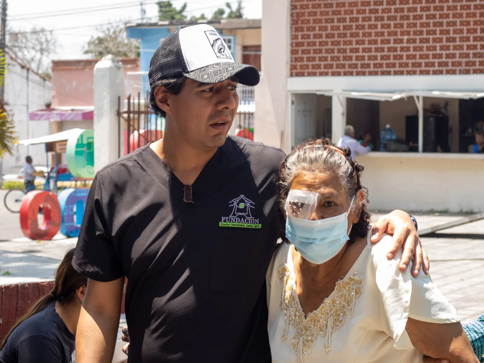 Integrante del equipo abraza por los hombros a una paciente con protector ocular